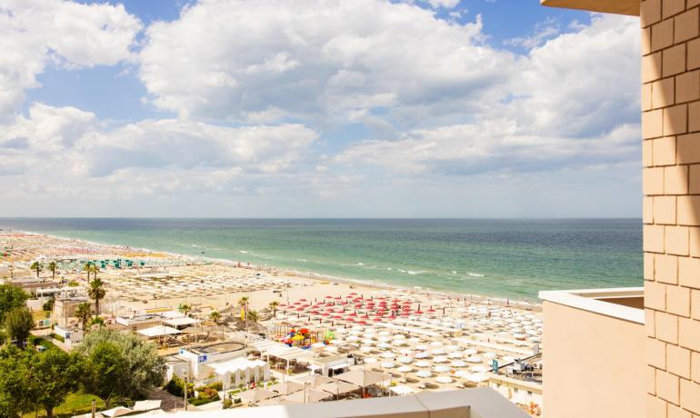 Meerblick mit Strand und bunten Sonnenschirmen unter einem wolkigen Himmel.