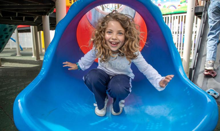 Fröhliches Kind rutscht auf einer bunten Rutsche im Spielplatz.
